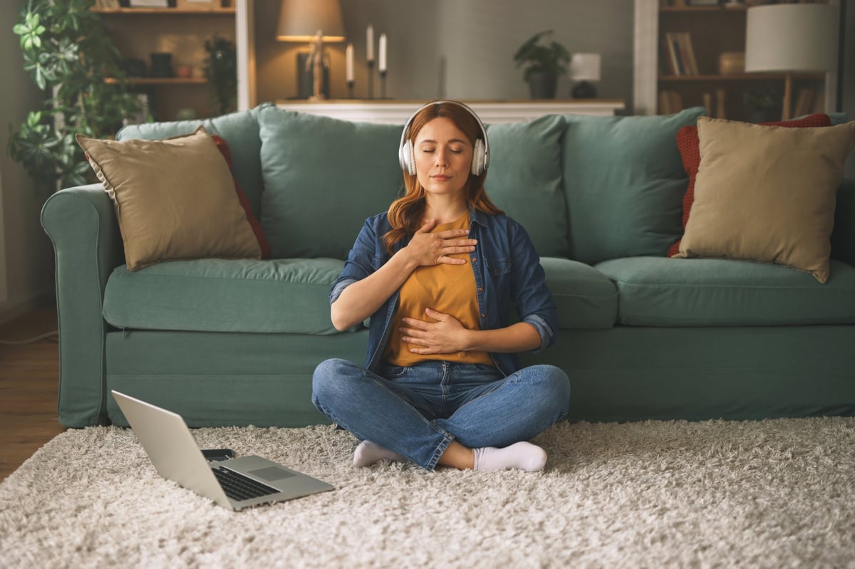 A calm woman meditating in her living room, hands resting gently at heart level