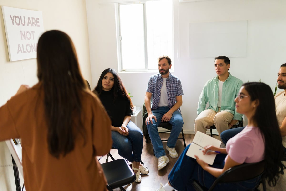 Group of people sitting in a circle listening to a counselor leading a workshop session
