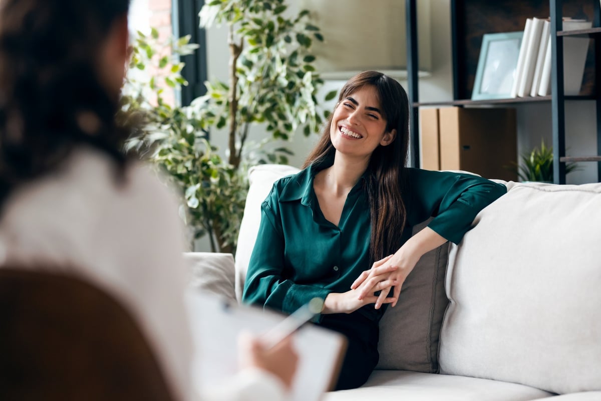 A woman in therapy, sitting comfortably while her therapist listens and takes notes