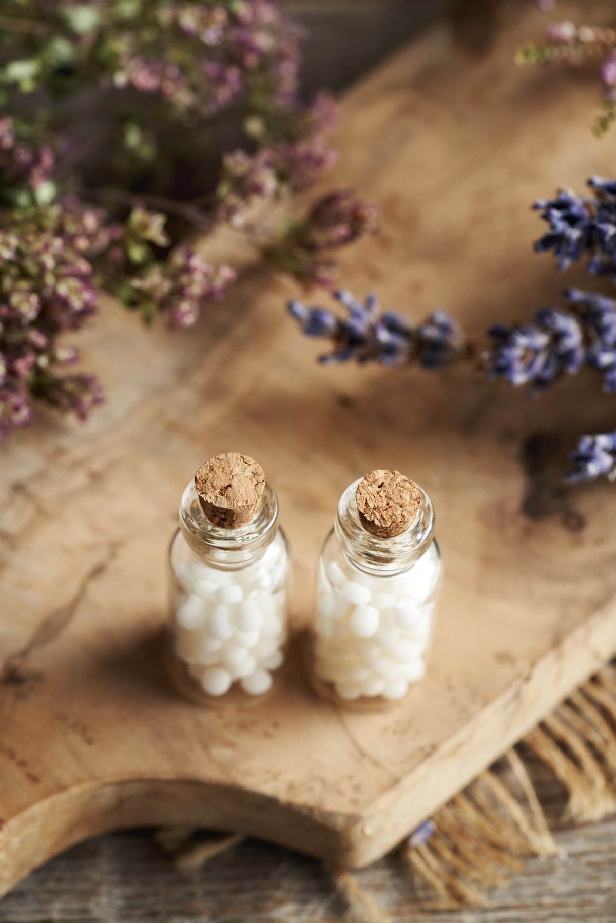 Two bottles of homeopathic pills with dried flowers and herbs on a warm surface