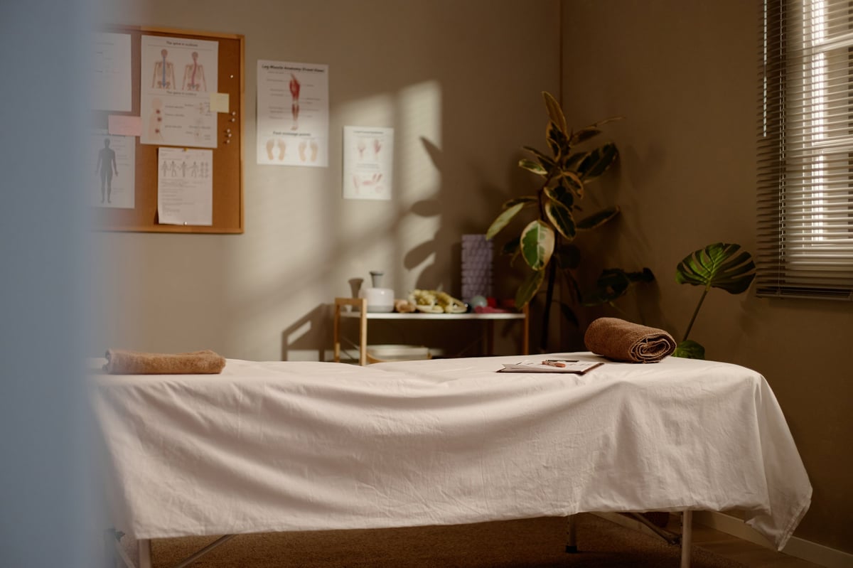 Professional treatment room with massage table, towels, and anatomy charts in warm natural light