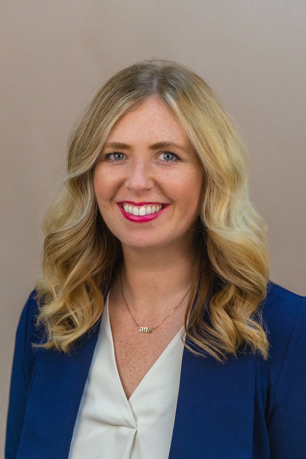Portrait of Keely Puchalski, a blonde woman wearing a navy blazer and white blouse, smiling at the camera