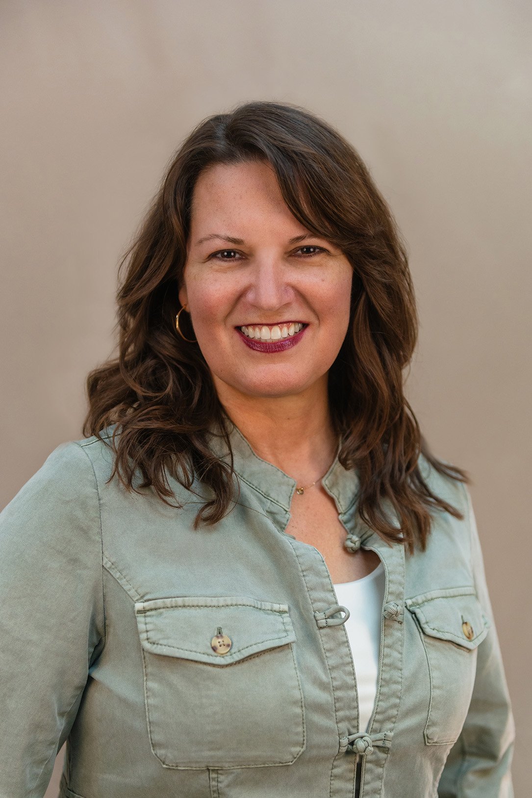 Portrait of Tiffany Cramer, a smiling woman with long brown wavy hair wearing a light blue denim shirt