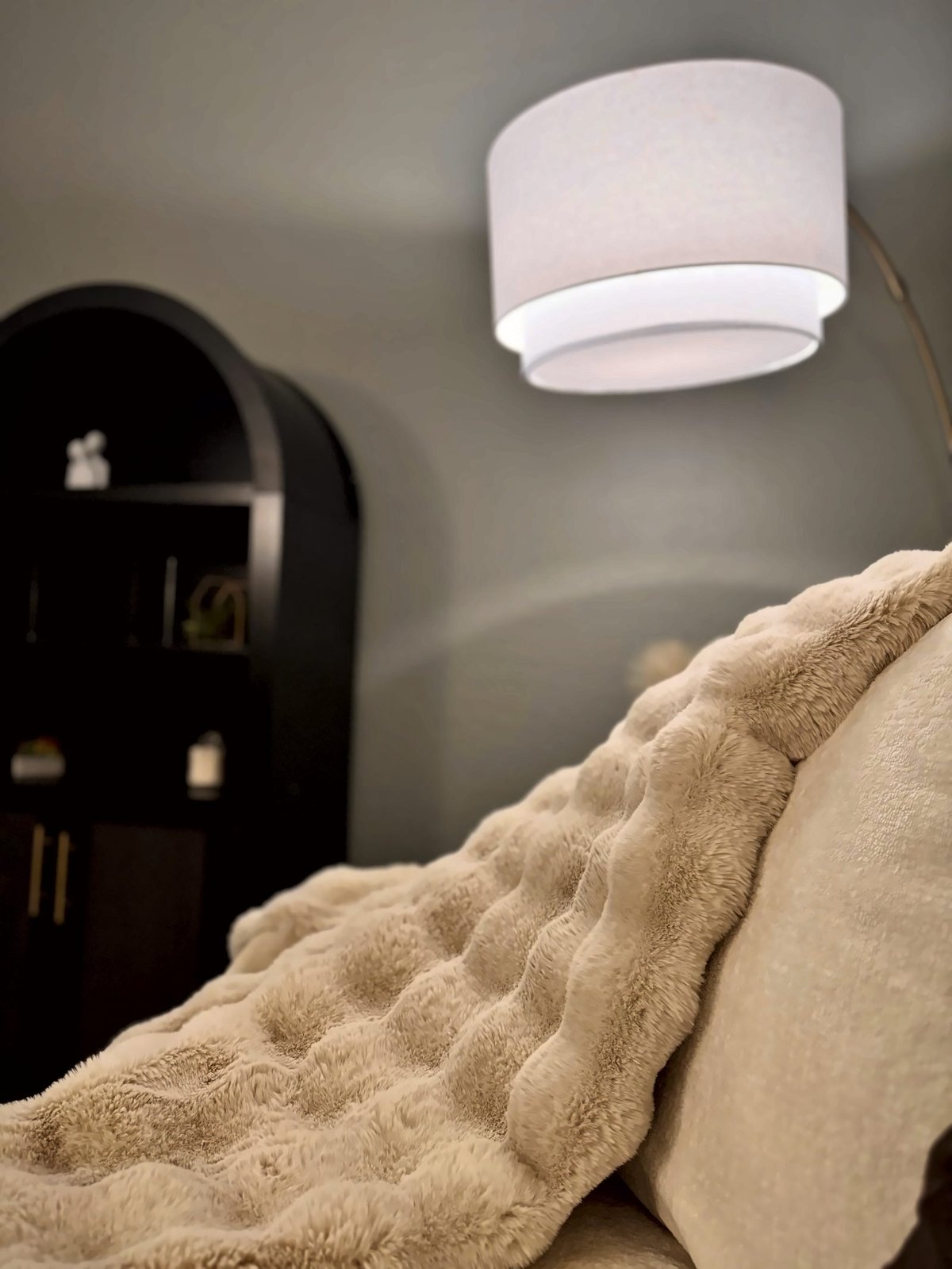 Beige cushioned chair with cream blanket draped over it, beside a dark wooden side table and white ceiling light