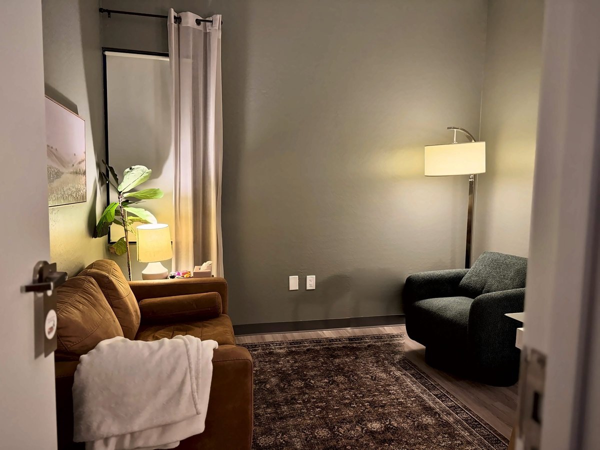 Modern bedroom with brown leather chair, black armchair, wall-mounted mirror, potted plant, floor lamp, and textured area rug