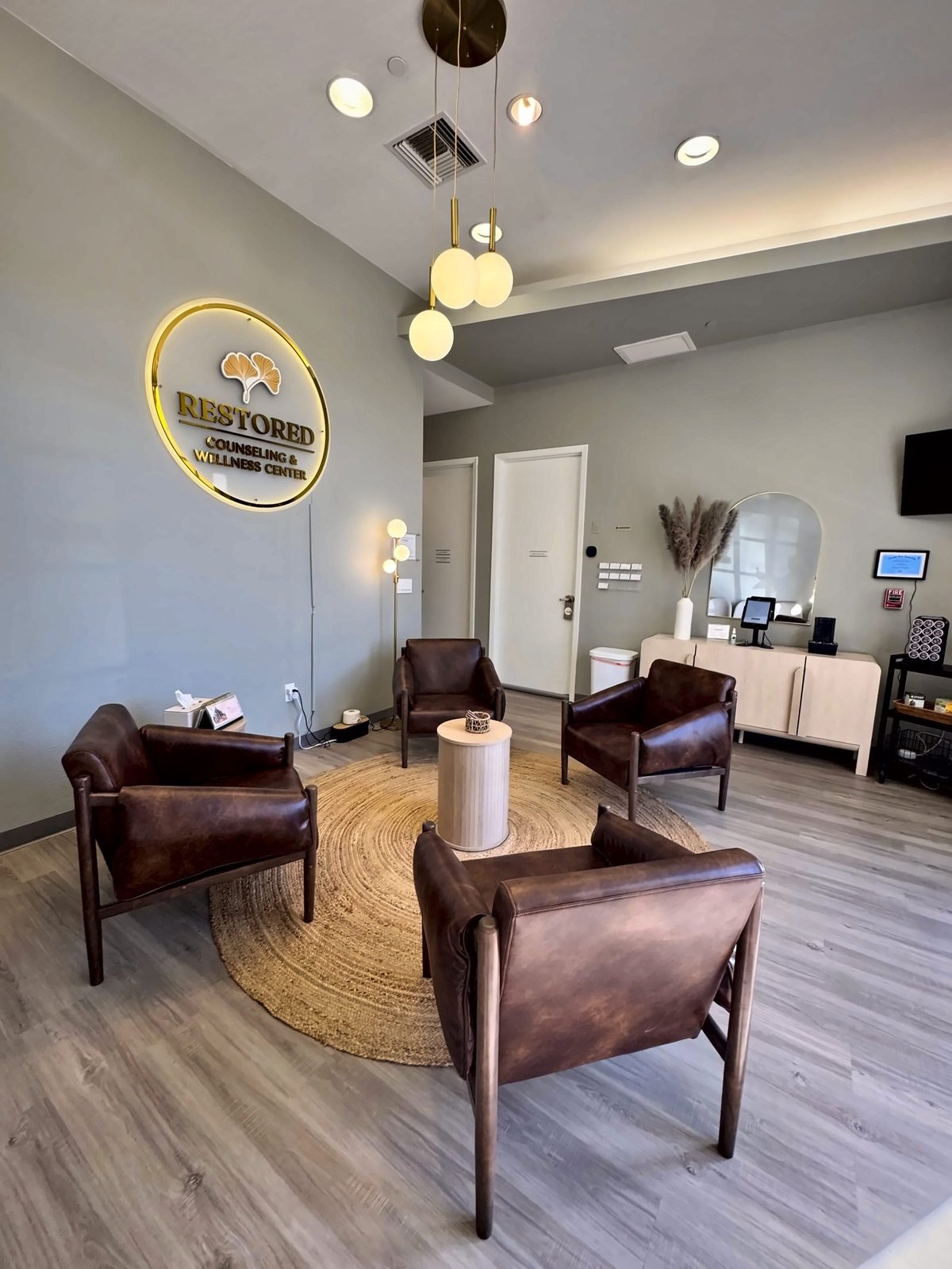 Modern salon reception area with brown leather chairs, round rug, pendant lighting, and neon sign on gray walls